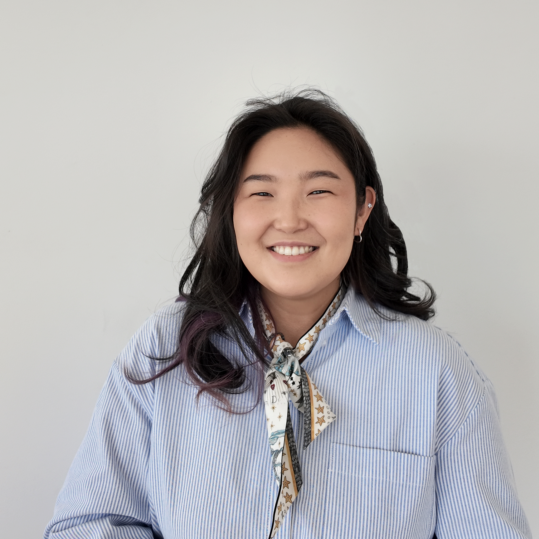 Portrait of a person smiling and wearing a striped shirt with a scarf.