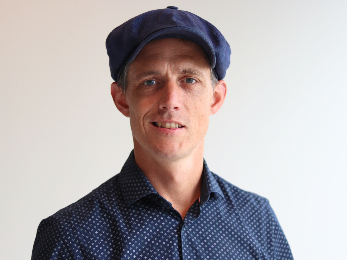 Portrait of a person wearing a cap and collared shirt.