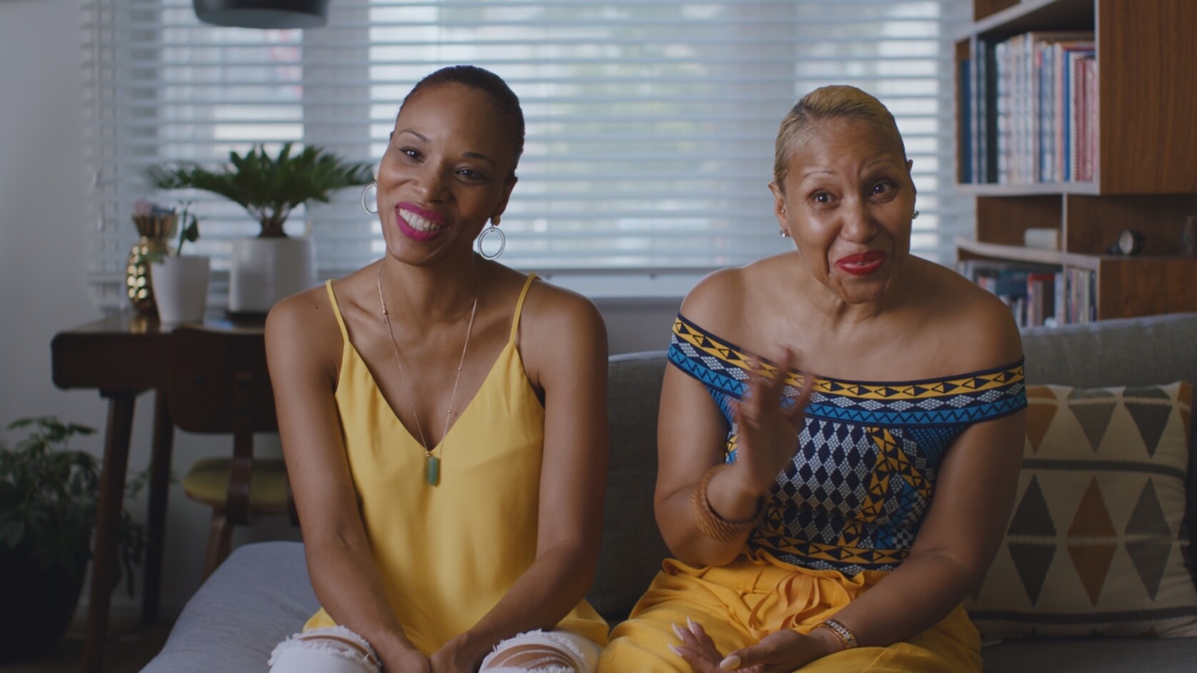 Two women sitting a couch will taking and smiling