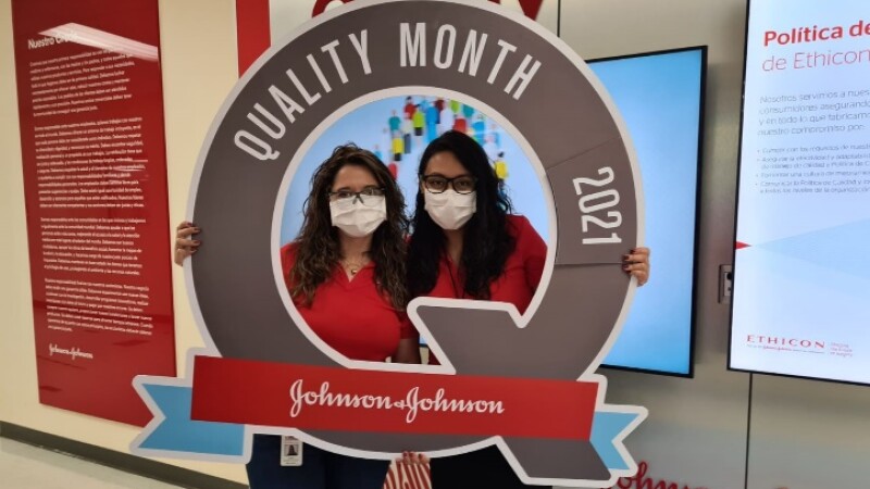 Two women stand in behind a sign that reads Quality Month 2021 Johnson & Johnson